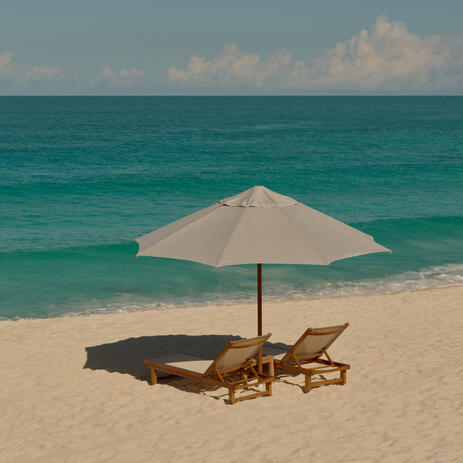 Two beach chairs under an umbrella on pristine white sand at Amanyara